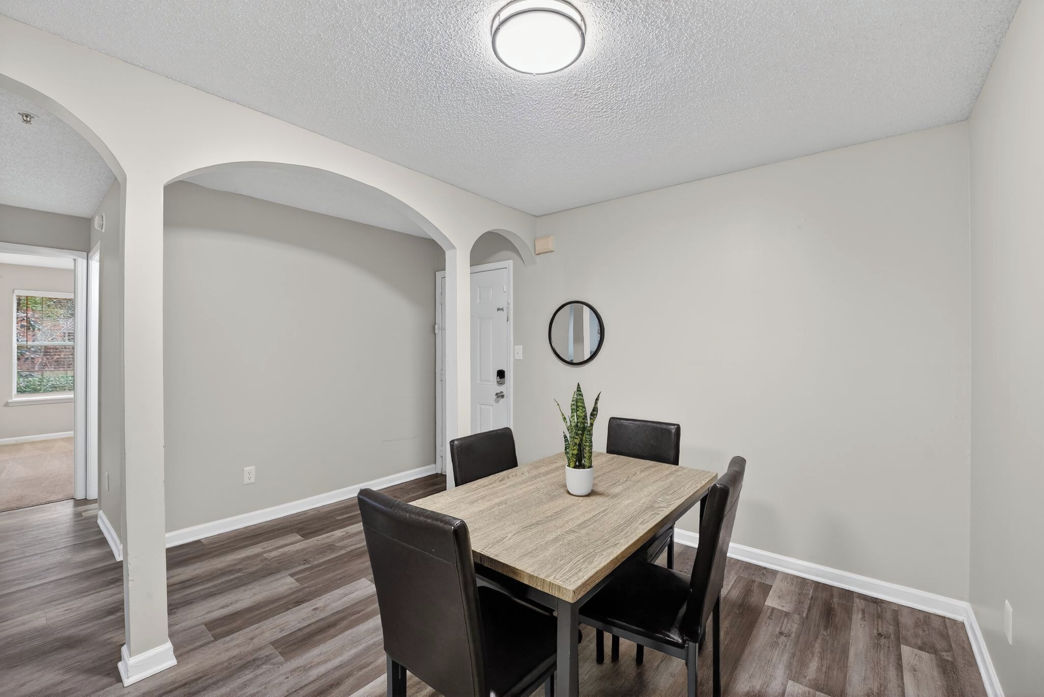 A dining area with a wooden table, black chairs, a potted plant, and a mirror on the wall.