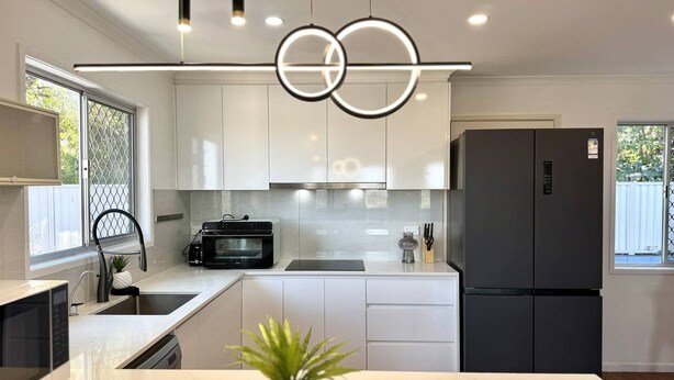 Une cuisine moderne avec des meubles blancs, un réfrigérateur noir et un îlot central agrémenté d’une plante.
