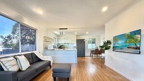 Un espace de vie moderne avec un canapé gris, un plancher en bois, un îlot de cuisine et une grande fenêtre.