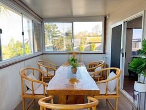 Une terrasse couverte avec une table et des chaises en bois, une plante en pot et une vue sur l’extérieur.