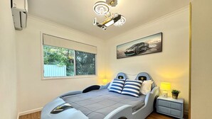 Une chambre moderne avec un lit au design original sur le thème de l’automobile, une grande fenêtre et un luminaire au plafond.