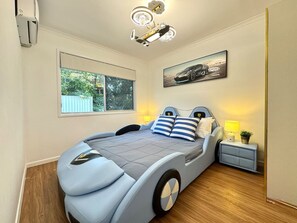 Une chambre moderne avec un lit au design original sur le thème de l’automobile, une grande fenêtre et un luminaire au plafond.