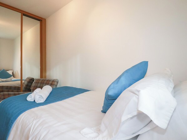 A hotel room with a bed, a mirror, and a view of another room.