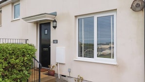 A residential building with a black door, a window with blinds, and a small garden area with potted plants. - Blissful Ocean Breeze (Perranporth)