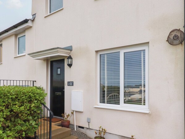 A residential building with a black door, a window with blinds, and a small garden area with potted plants. - Blissful Ocean Breeze (Perranporth)