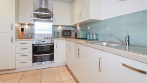 A modern kitchen with white cabinets, stainless steel appliances, a microwave, a kettle, and a sink. - Blissful Ocean Breeze (Perranporth)
