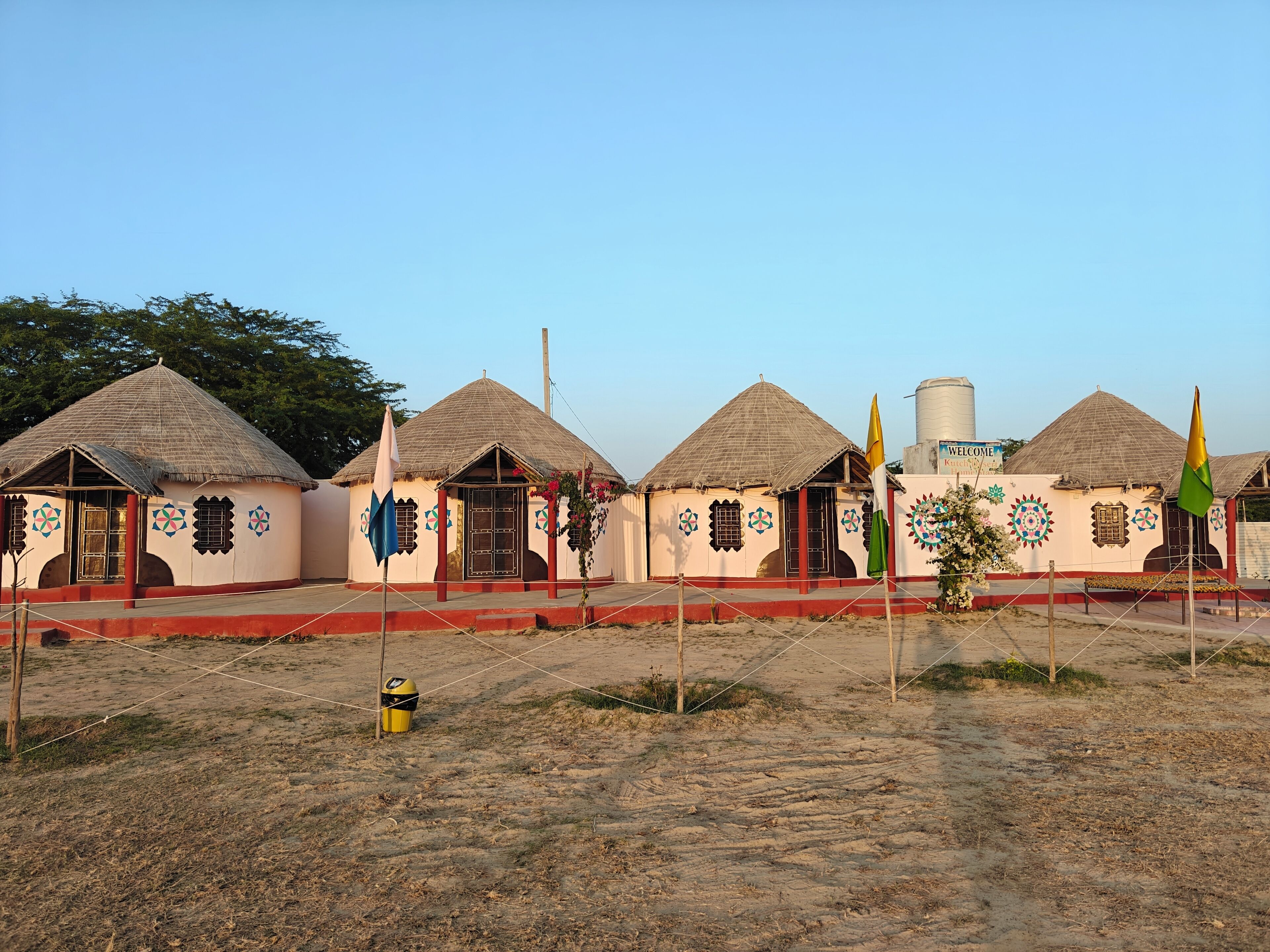 A row of traditional huts with thatched roofs and decorative patterns, surrounded by a fenced area with a clear sky.