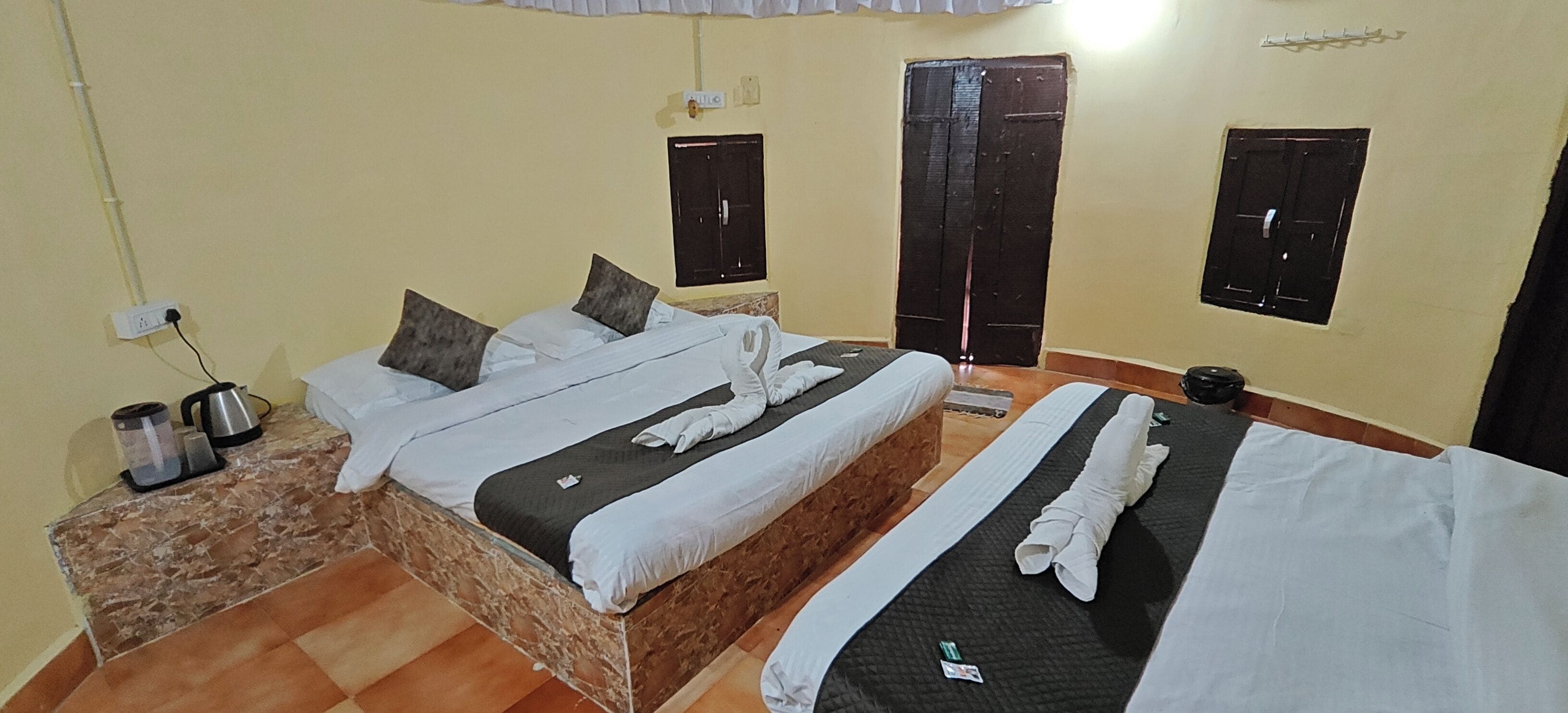 A hotel room with two beds, a marble bedside table, a coffee maker, and a wardrobe.