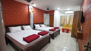 A hotel room with two beds, a TV, a ceiling fan, and a small table with chairs. - Coco Garden Residency (Bhatkal)