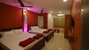 A hotel room with two beds, a small table, a bench, a ceiling fan, and a shower area. - Coco Garden Residency (Bhatkal)