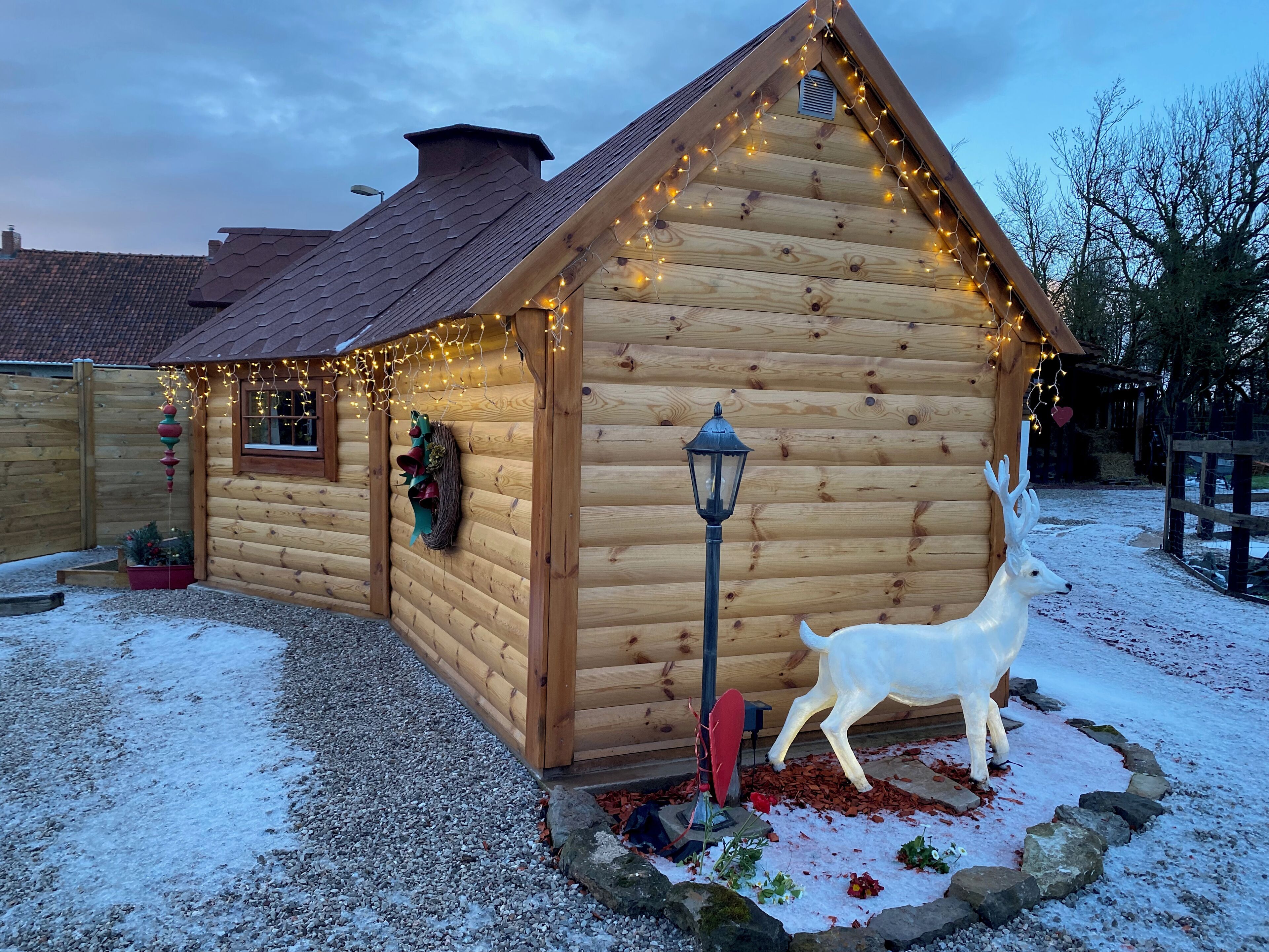 Una cabaña de madera con techo inclinado, luces colgantes, un farolillo y una estatua de ciervo.