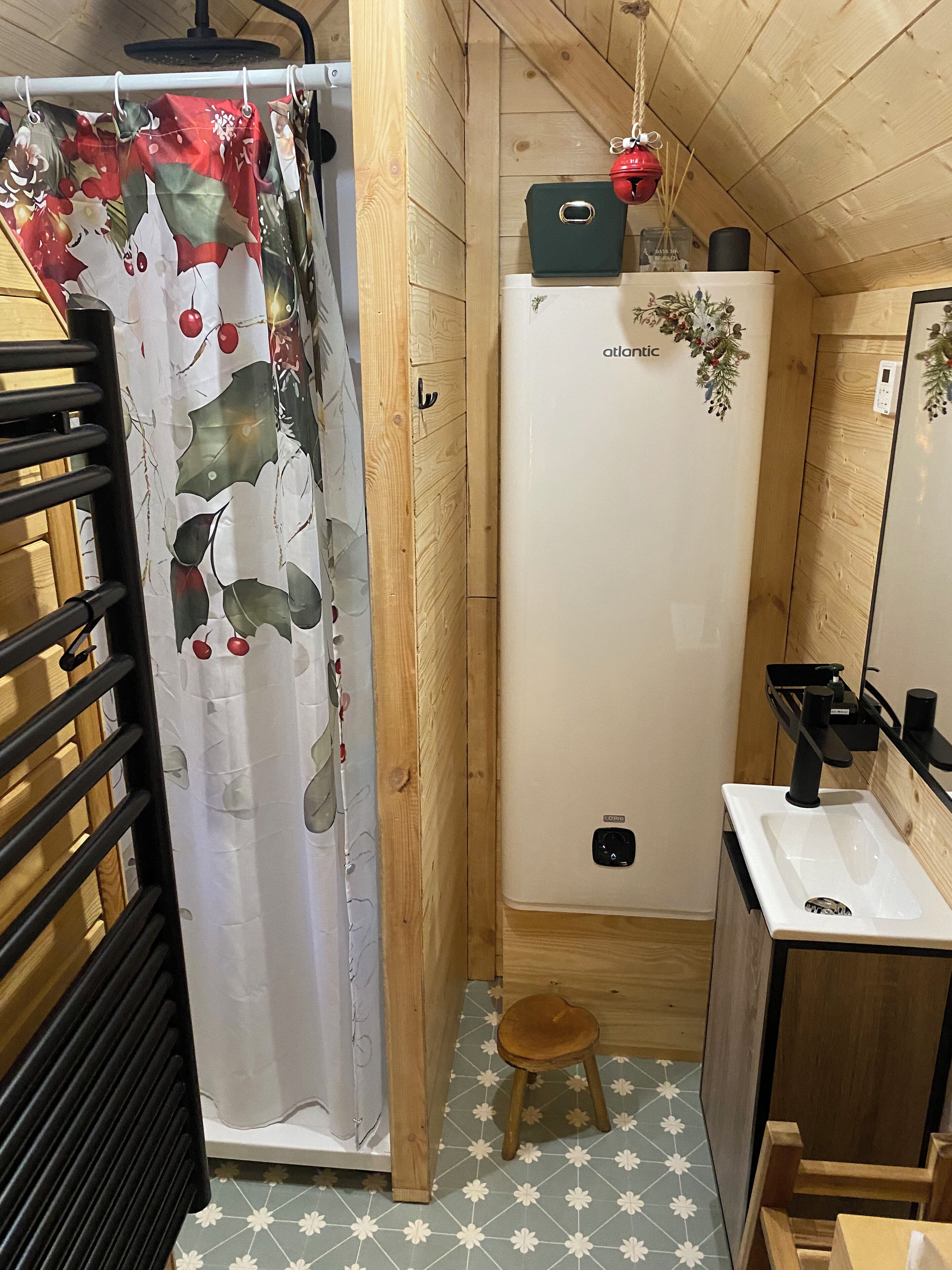 Et lille badeværelse med bruseforhæng, vask, toilet og en lille skammel.