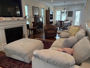 A living room with a fireplace, a television, a dining area with a table and chairs, and a large sofa with multiple cushions. -  5-bedroom house Ocean Grove 1.5 blocks to beach (Neptune Township)