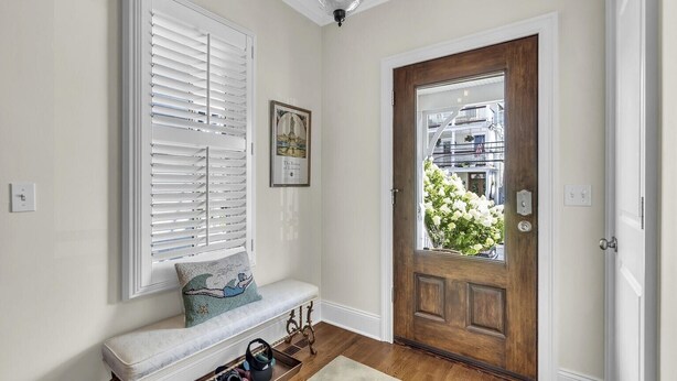 Una entrada limpia y bien iluminada con una puerta de madera, un banco con cojín y un cuadro en la pared.