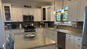 Una cocina moderna con armarios blancos, encimera de granito, electrodomésticos de acero inoxidable y un salpicadero decorativo.