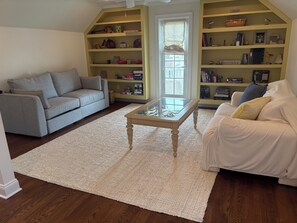 A living room with a grey sofa, a white sofa, a glass-top coffee table, and a bookshelf filled with various items. -  5-bedroom house Ocean Grove 1.5 blocks to beach (Neptune Township)