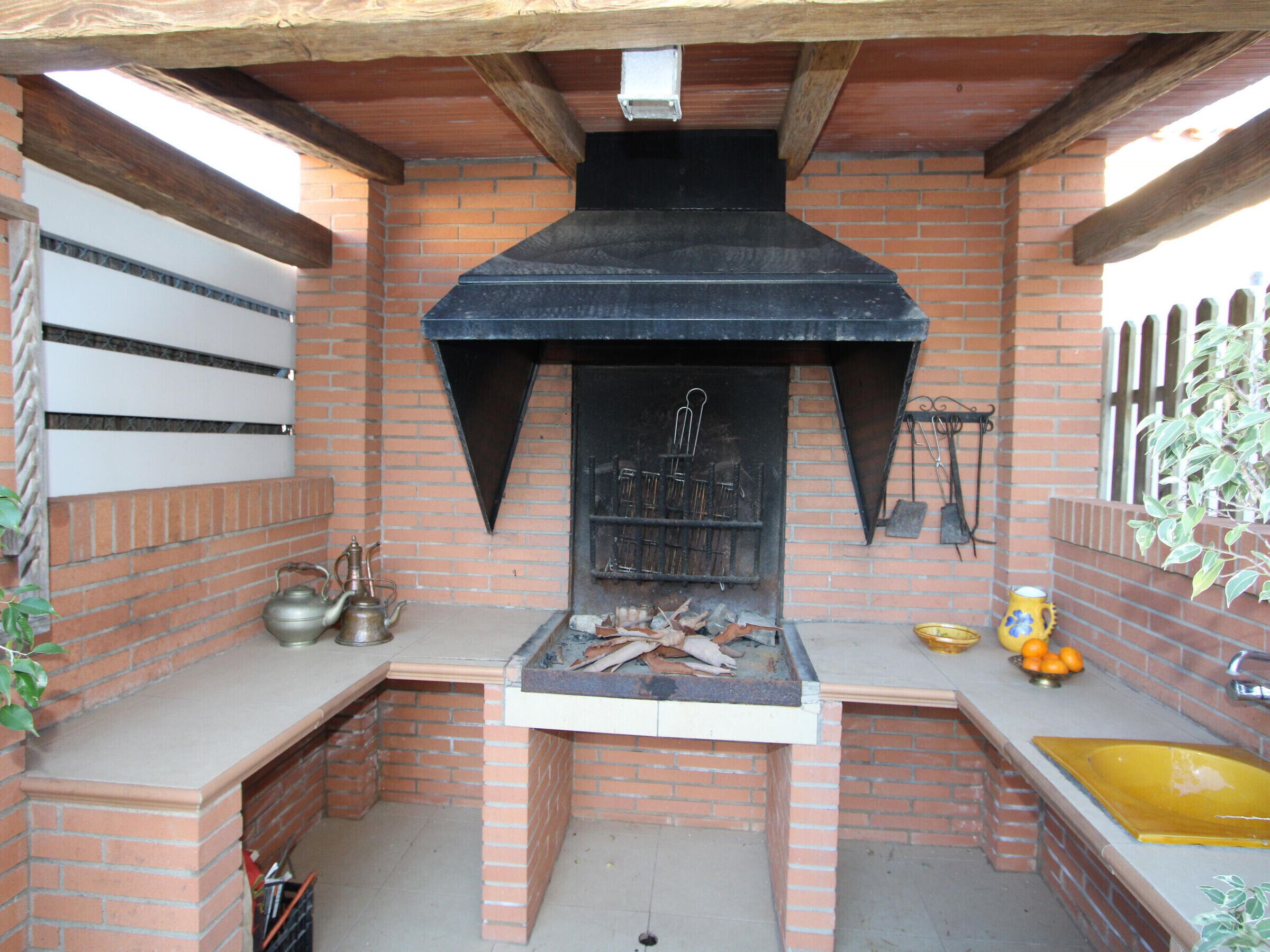 A brick-built outdoor kitchen with a chimney, a sink, and a shelf with kitchen utensils.