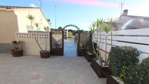Um pátio pavimentado com um portão, plantas em vasos e um edifício com telhado de azulejos.