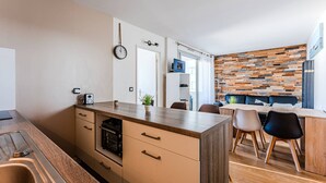 A modern kitchen with a wooden countertop, built-in oven, and a sink. There is a dining area with a wooden table and chairs, and a wall with a wooden panel design. - Arcachon Aiguillon: 2-Bedroom with Balconies and Parking (Arcachon)