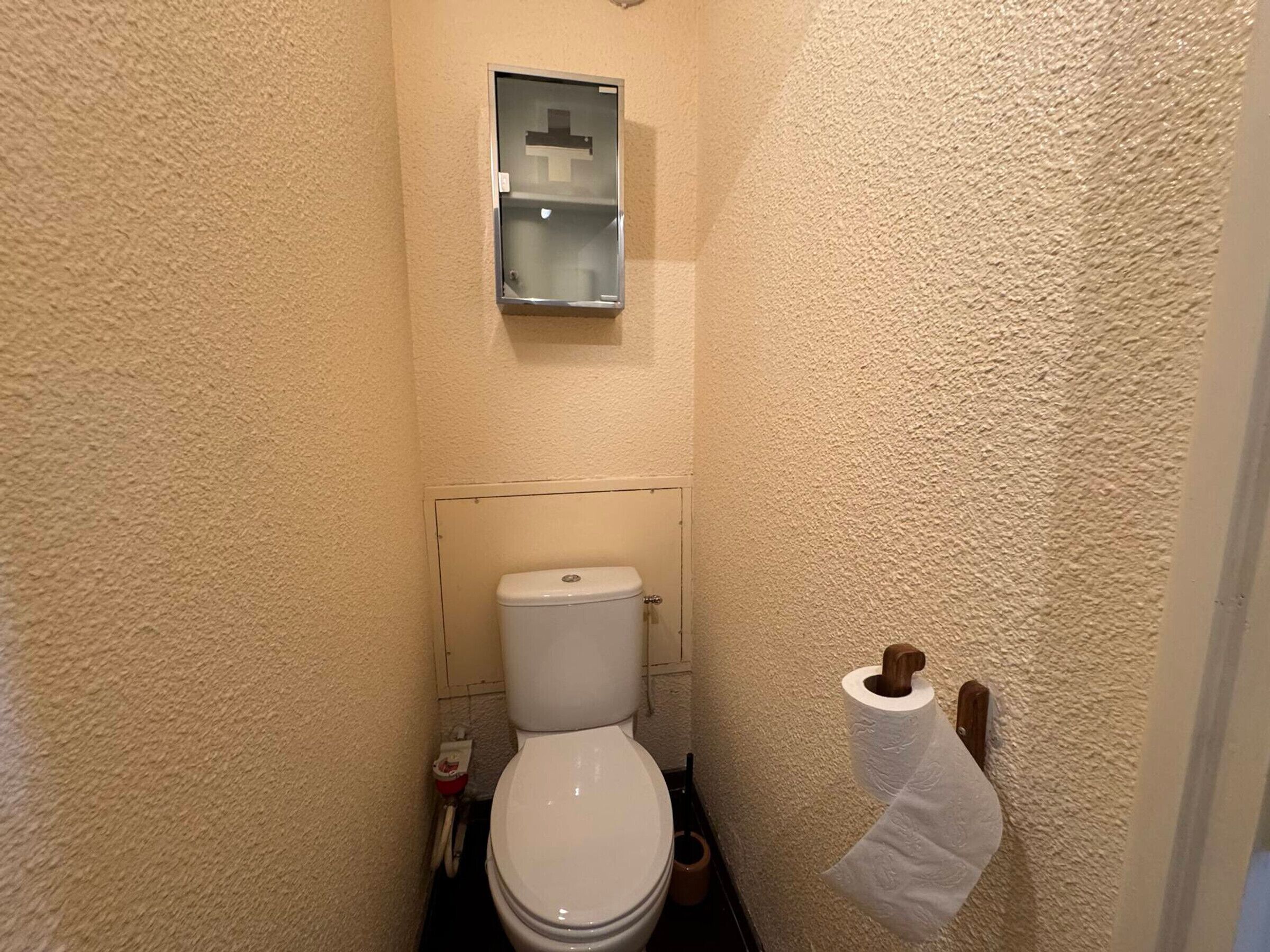 Pieni, kapea kylpyhuone, jossa on wc, wc:n yläpuolella pieni hylly ja seinällä wc-paperiteline.