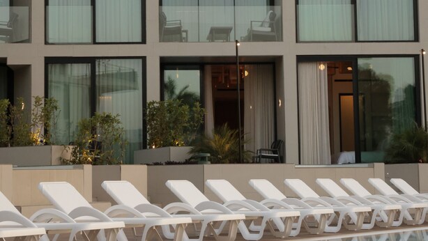 A modern hotel with a pool area, featuring multiple lounge chairs and a clear view of the surrounding landscape. - Inanna Resort  (Batroun)