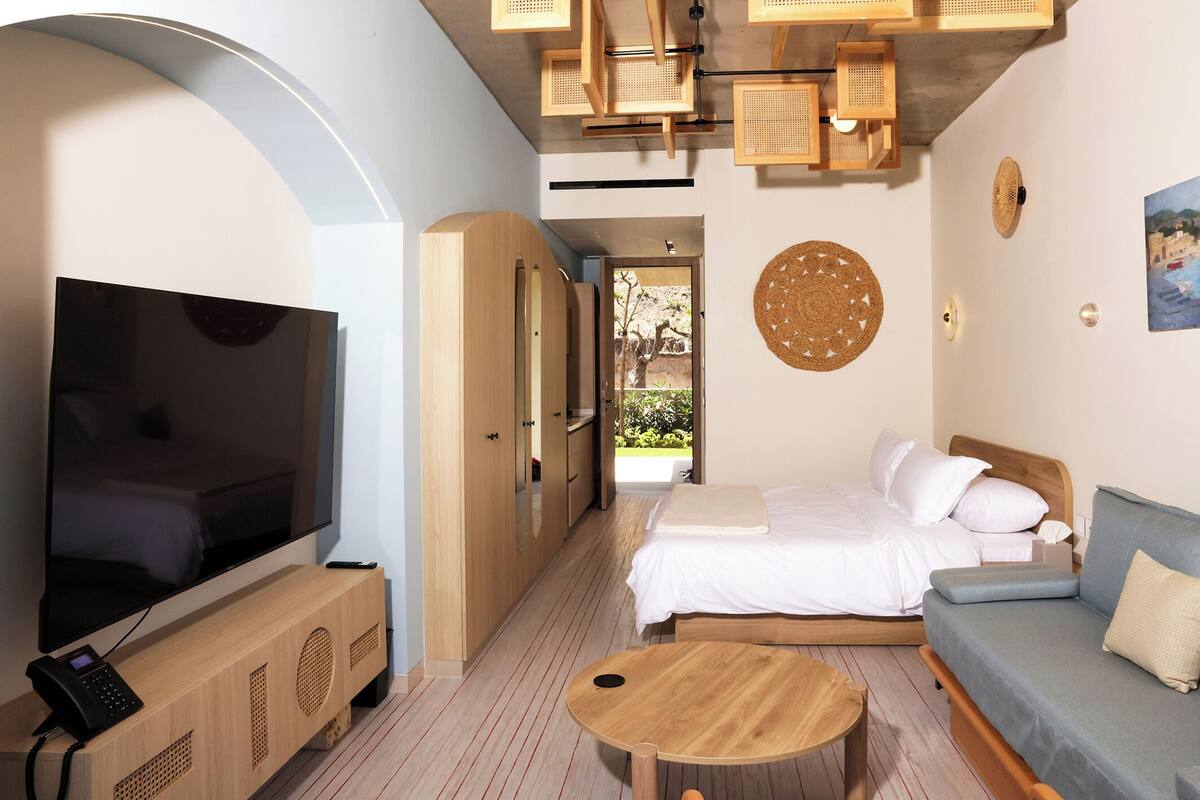 A hotel room with a TV, wooden furniture, a bed, a sofa, and a small table.