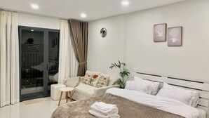 A modern bedroom with a large bed, a small seating area, and a sliding glass door leading to a balcony. - Spacious Luxury City View with Pool - Korean Town, closed by City center & SECC (Thành phố Hồ Chí Minh)