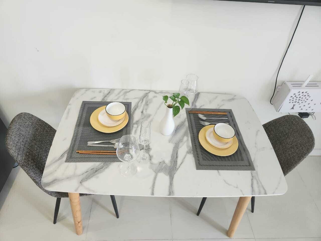 A dining table with a marble top, two chairs, and a vase with a plant.