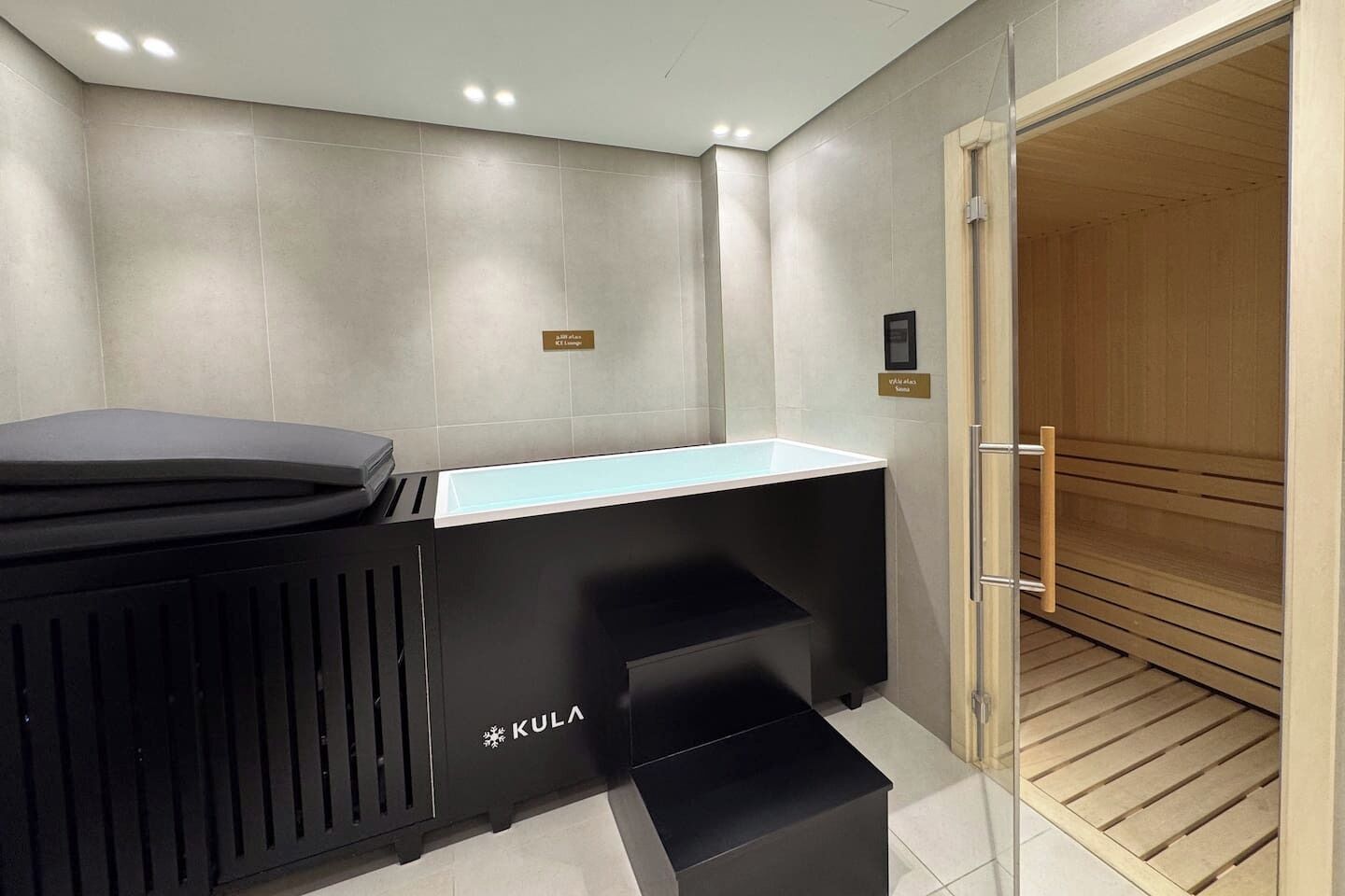 Une salle de bain moderne avec un meuble-lavabo noir, un évier et une porte en bois menant à un sauna.
