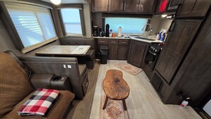 A compact RV kitchen with a dining area, a small table, and a bench. - Cozy RV at Rocky Creek Ranch Hot Tub Pet Private (Fredericksburg)