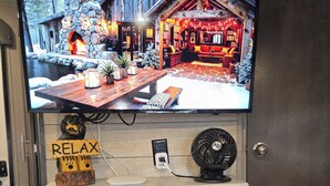 A fireplace with a TV mounted above it displaying a cozy cabin scene. - Cozy RV at Rocky Creek Ranch Hot Tub Pet Private (Fredericksburg)