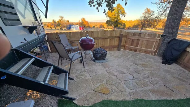 A backyard with a barbecue grill, outdoor seating, and a stone patio. - Cozy RV at Rocky Creek Ranch Hot Tub Pet Private (Fredericksburg)