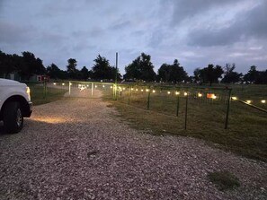 Ein Schotterweg führt zu einem eingezäunten Bereich mit Lichterketten.