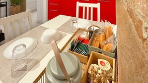 A kitchen with red cabinets, a white countertop, and a dining area with a table set for two. - Casa Alleria - Cozy Venetian Apartment in Cannaregio, near Rialto Bridge (Venezia)