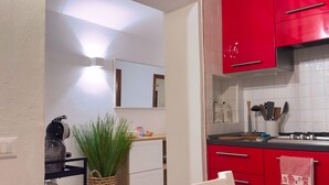 A kitchen with red cabinets, a white countertop, and a clock on the wall. - Casa Alleria - Cozy Venetian Apartment in Cannaregio, near Rialto Bridge (Venezia)