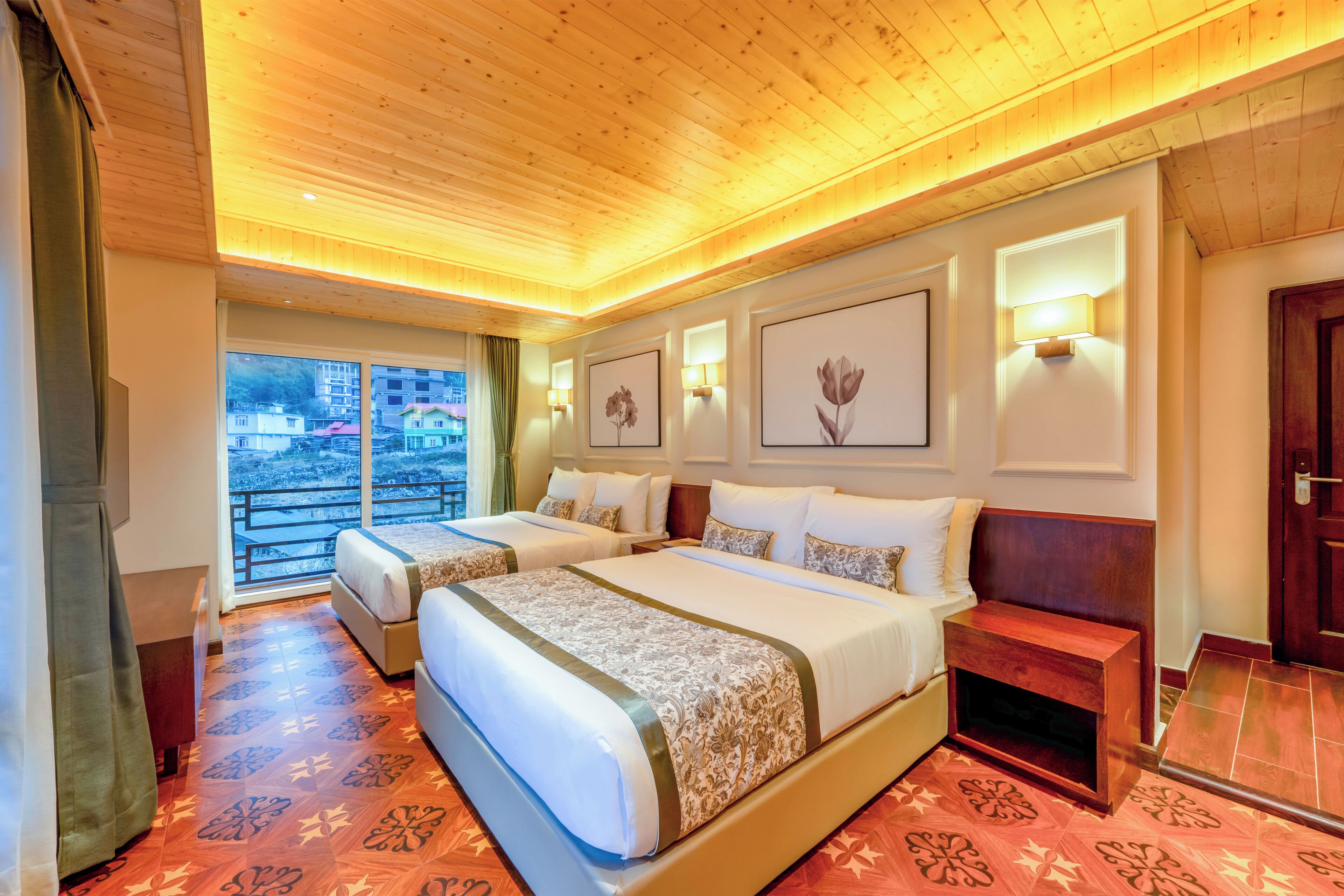 Habitación de hotel con dos camas, techo de madera, balcón con vistas y cuadros en las paredes.