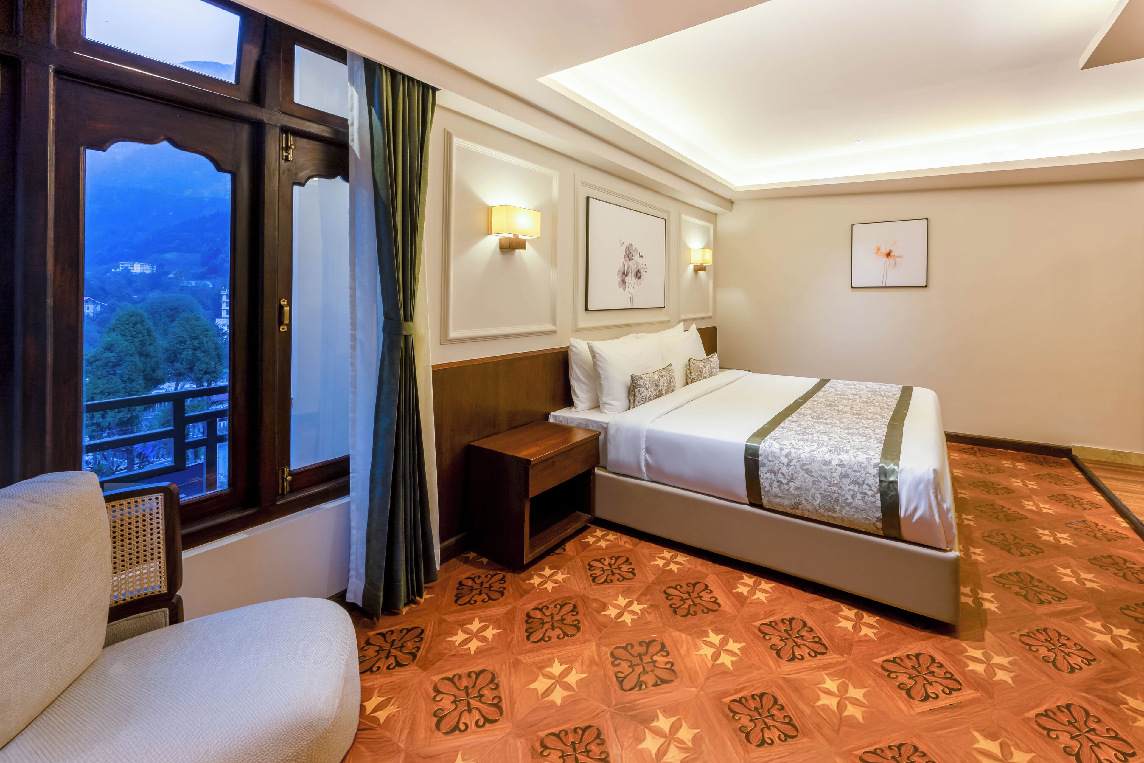 A hotel room with a bed, a nightstand, a chair, a window with a view, and wall-mounted lights.