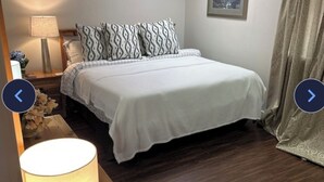 Quarto bem arrumado com cama, abajur, quadro na parede e cortina.