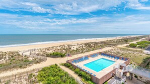 Ein Pool am Strand mit blauen Stühlen, einem Sandstrand und dem Ozean im Hintergrund.