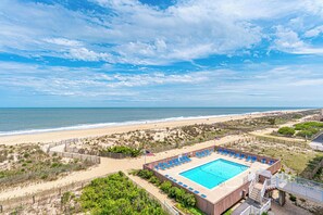 A beachside pool with blue chairs, a sandy beach, and the ocean in the background. - Beautiful remodel one Bedroom Ocean Front with outdoor pool (Ocean City)