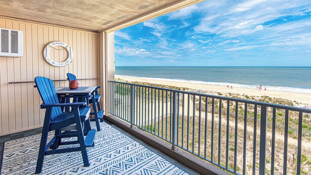 Ein Balkon mit Blick auf den Strand, ein Tisch mit Stühlen und einem Rettungsring an der Wand.