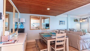 Ein modernes Wohnzimmer mit Holzboden, einem Essbereich mit Tisch und Stühlen, einer Couch und einer durch eine offene Tür sichtbaren Küche.