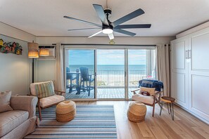 A room with a ceiling fan, a sofa, a chair, a small table, a woven ottoman, and a view of the ocean through large sliding doors. - Beautiful remodel one Bedroom Ocean Front with outdoor pool (Ocean City)