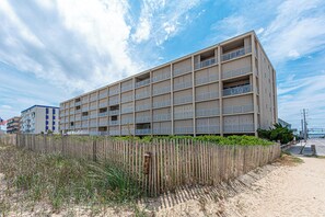 A multi-story building with balconies, a sandy beach in front, and a clear sky. - Beautiful remodel one Bedroom Ocean Front with outdoor pool (Ocean City)