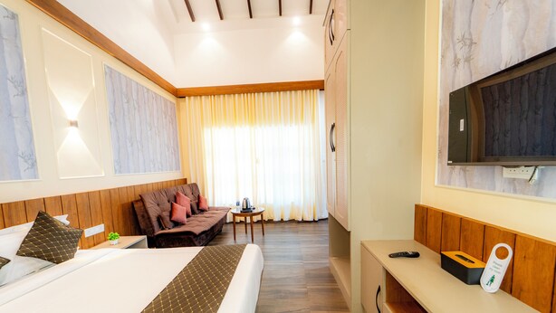 Une chambre d’hôtel avec un lit, un canapé, une petite table, une télévision et un banc en bois.