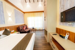 A hotel room with a bed, a sofa, a small table, a TV, and a wooden bench. - Nandanam Heritage Mahabaleshwar (Mahabaleshwar)