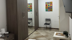 A bedroom with a bed, a wardrobe, a chair, a small table with a plant, and a wall with colorful artwork. - New Florence Smart Flat - Parking & Tram Stop (Firenze)