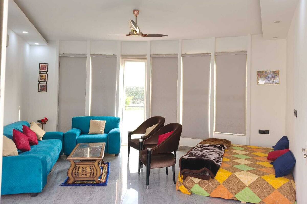 Una sala de estar moderna con un sofá azul, un sillón marrón, una mesa de centro de vidrio y una alfombra colorida.