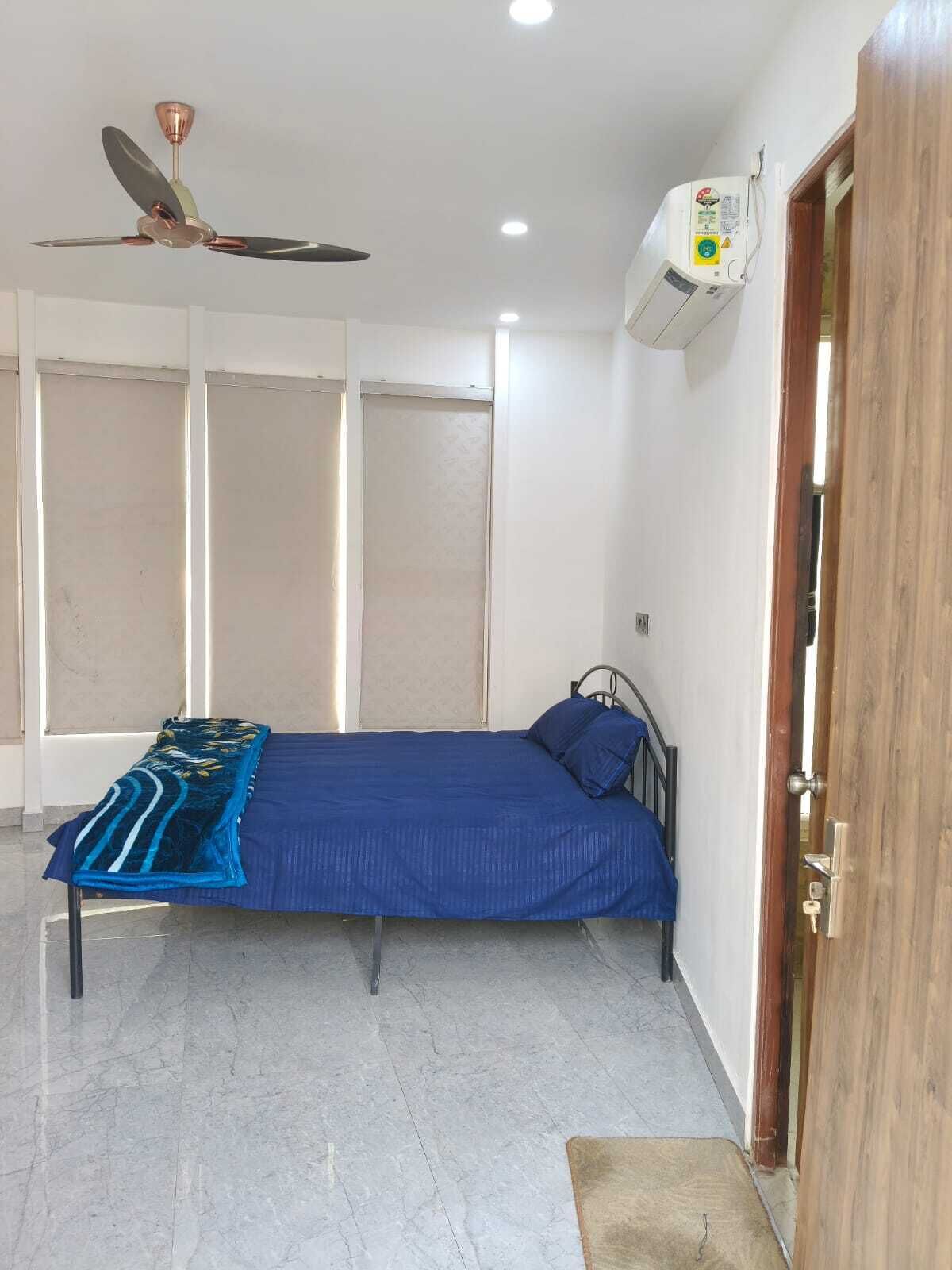 A bedroom with a bed, a ceiling fan, an air conditioning unit, and a wooden door.