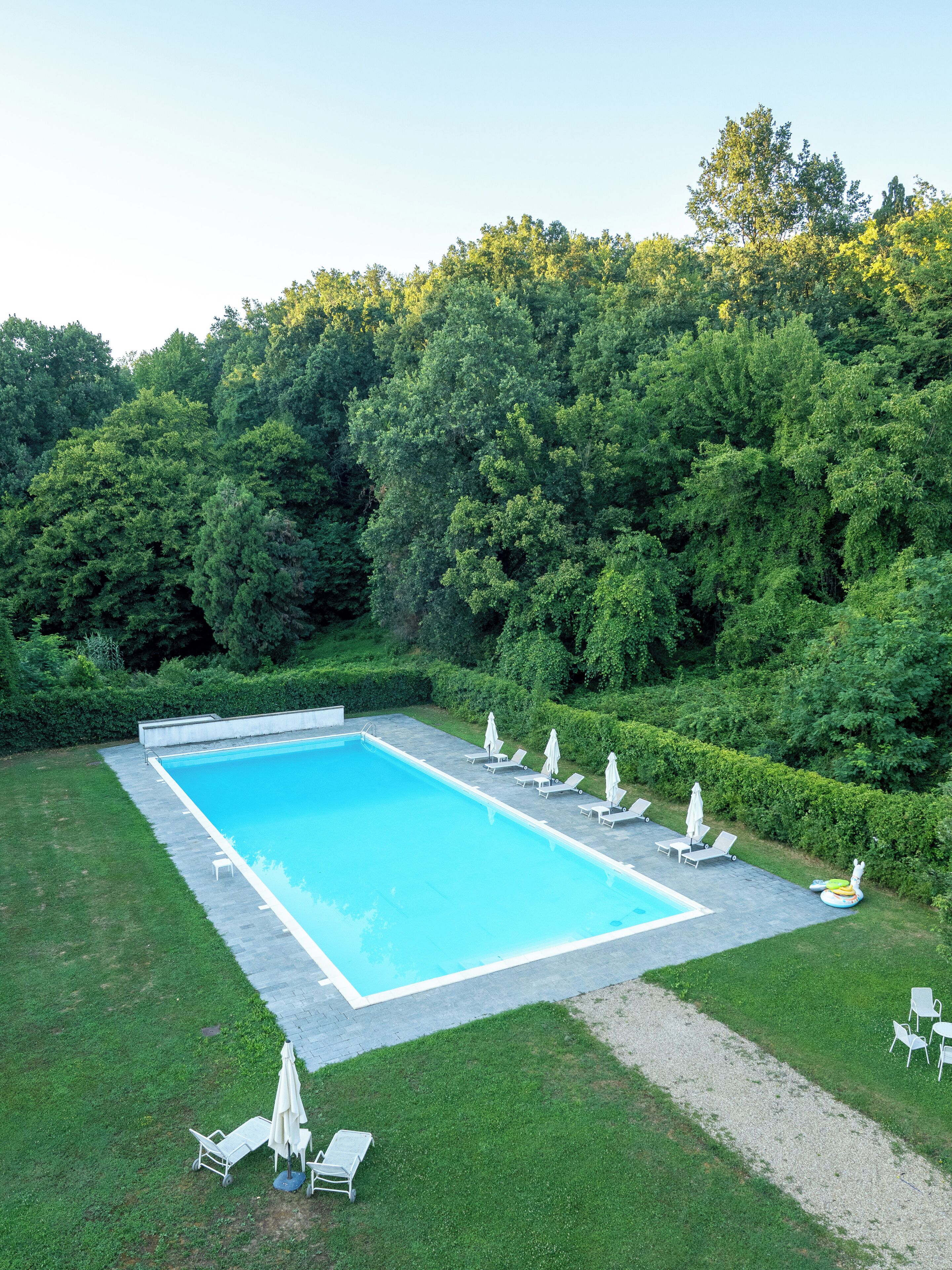 Una piscina rectangular con solárium empedrado, rodeada de césped y setos.